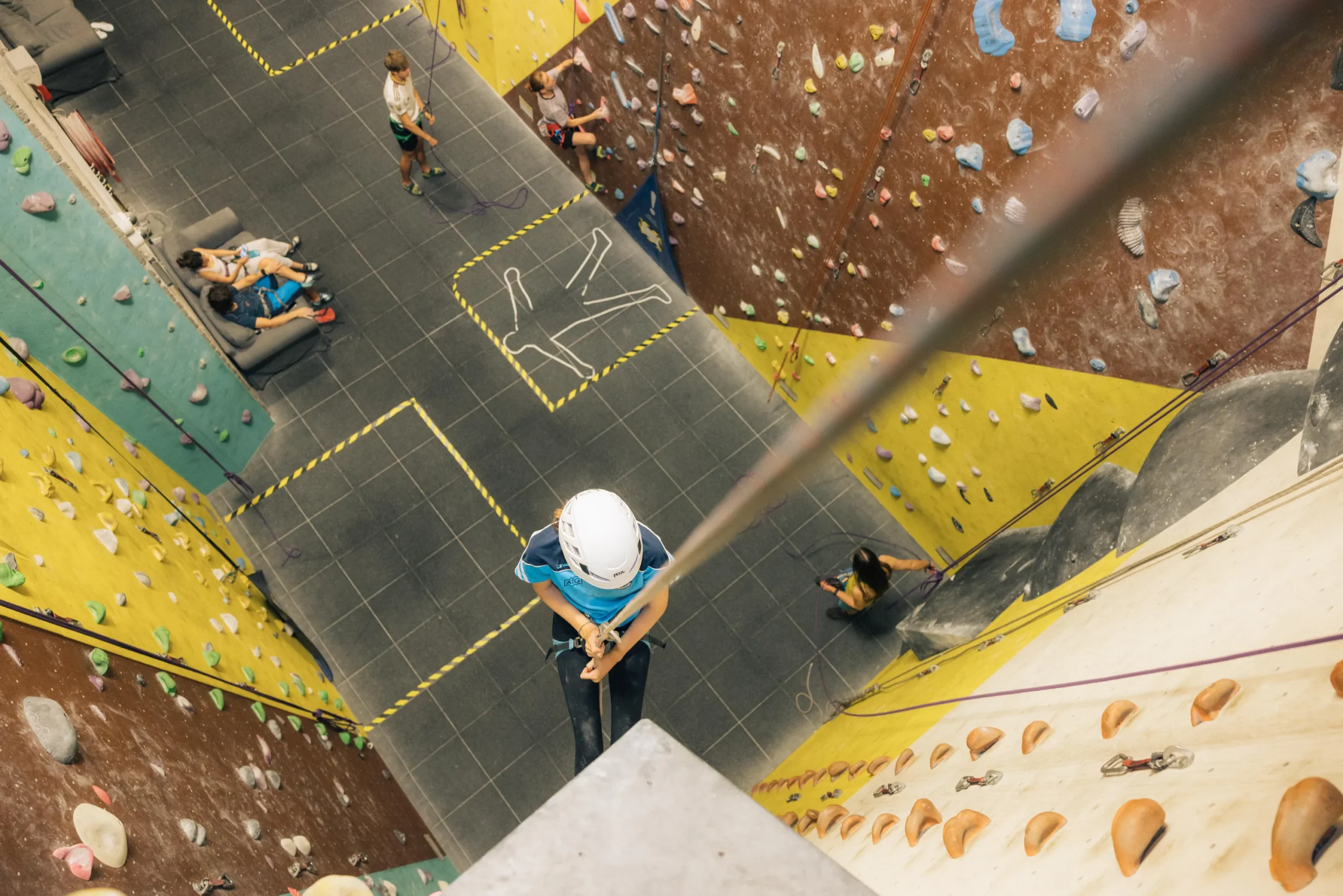 A child abseils a corner section at the Dublin Climbing Centre with other climbers in the background climbing and sitting on a sofa