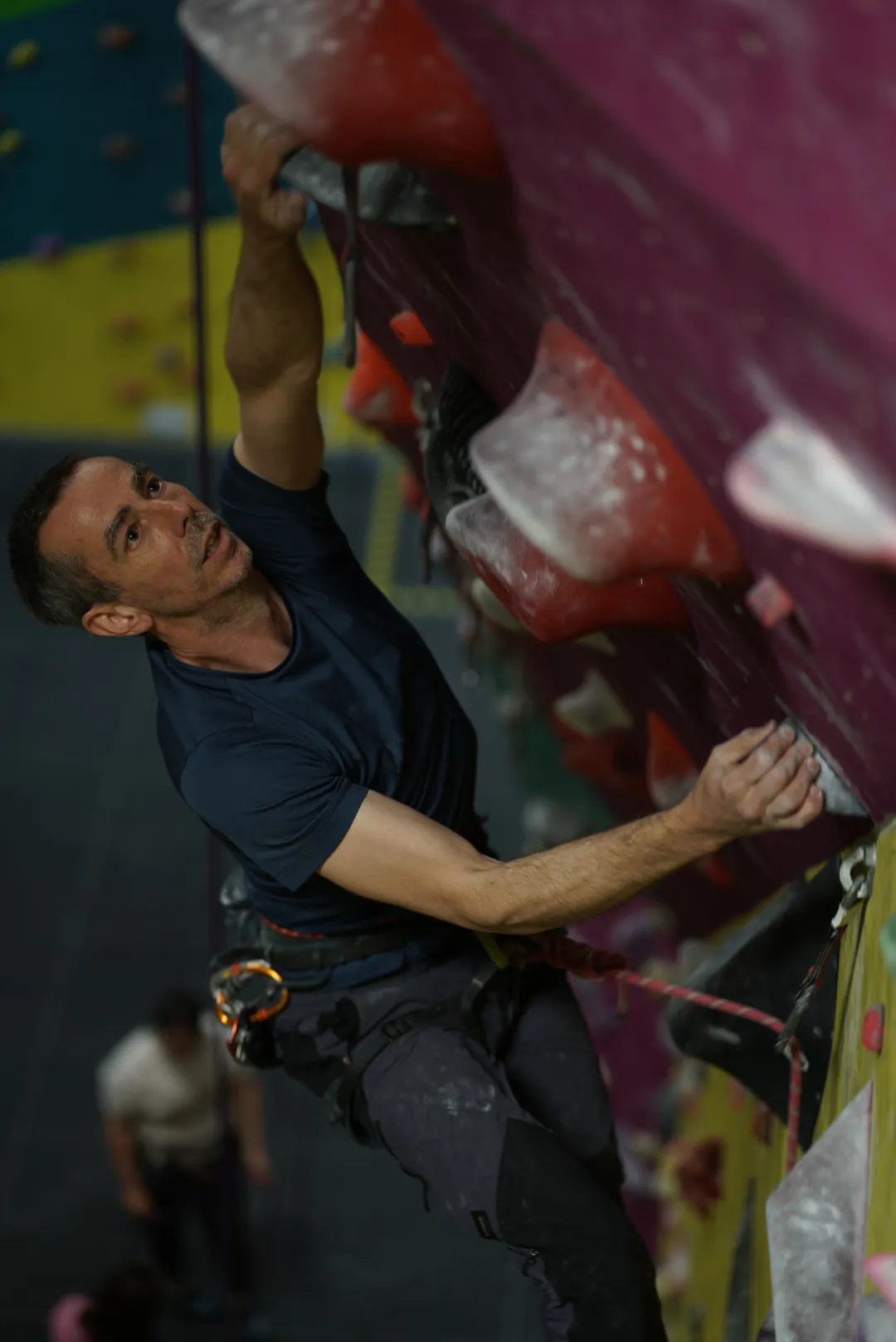 A male climber climbing and looking upwards towards the next quickdraw on a lead climbing route at Dublin Climbing Centre