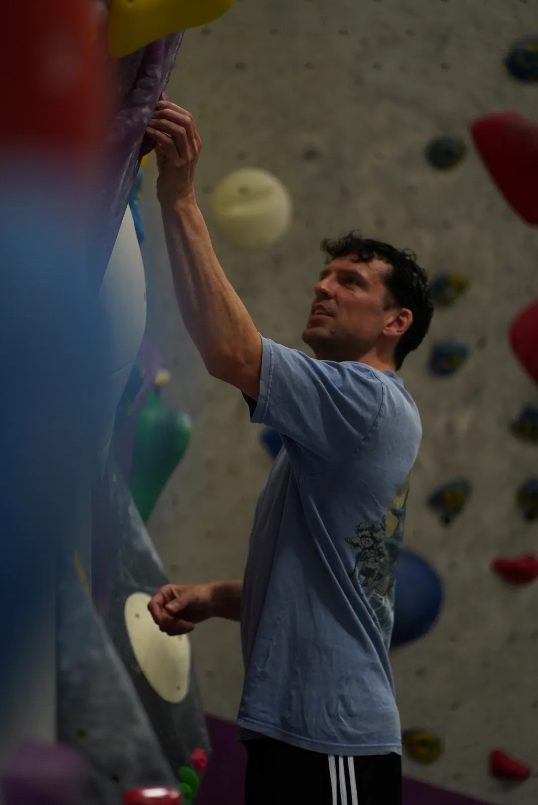 Tuesday Bouldering Workshop Coach Phil inspecting a crimp handhold on the bouldering wall at Dublin Climbing Centre