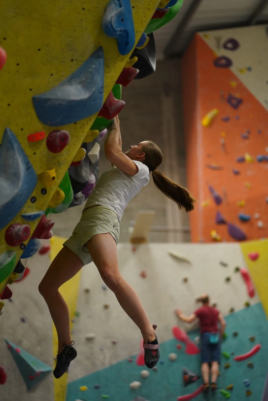 A female climber performing a dynamic jumping move on the boulder wall with her feet off the wall and hands on at Dublin Climbing Centre