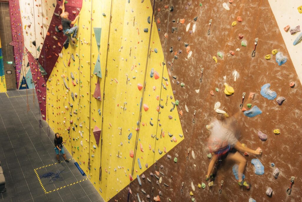 Climbers on a tall lead climbing wall with yellow and maroon panels at Dublin Climbing Centre