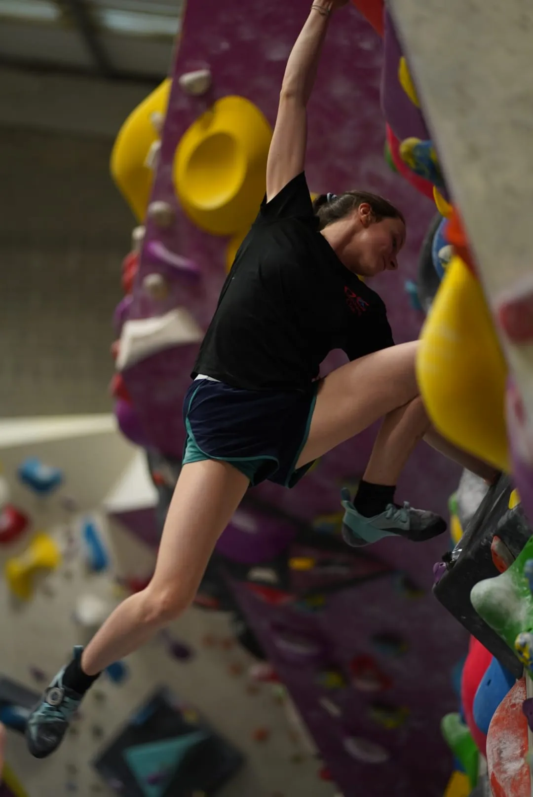 A woman boulder climbing performing a dynamic jumping move at Dublin Climbing Centre