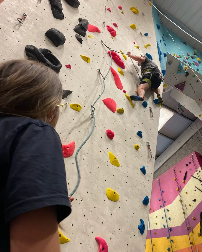 A belayer lead belaying a climber on the left side of the arch at Dublin Climbing Centre, with the lead climber visible on the wall behind