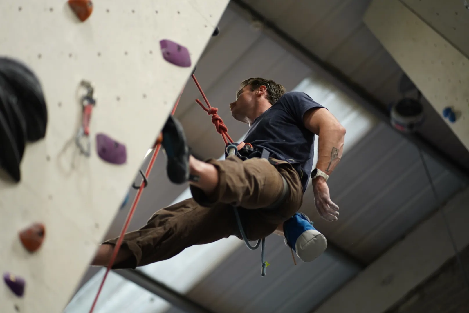 A lead climber resting on a route and reaching for his chalk bag at Dublin Climbing Centre