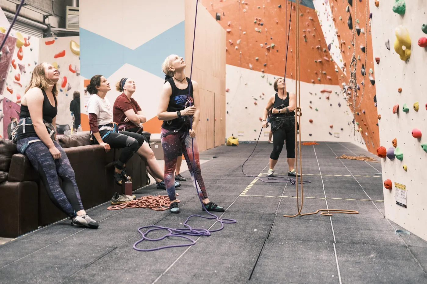 Ground view of two women belaying looking upward while another group also look up towards climbers on top-ropes at Dublin Climbing Centre