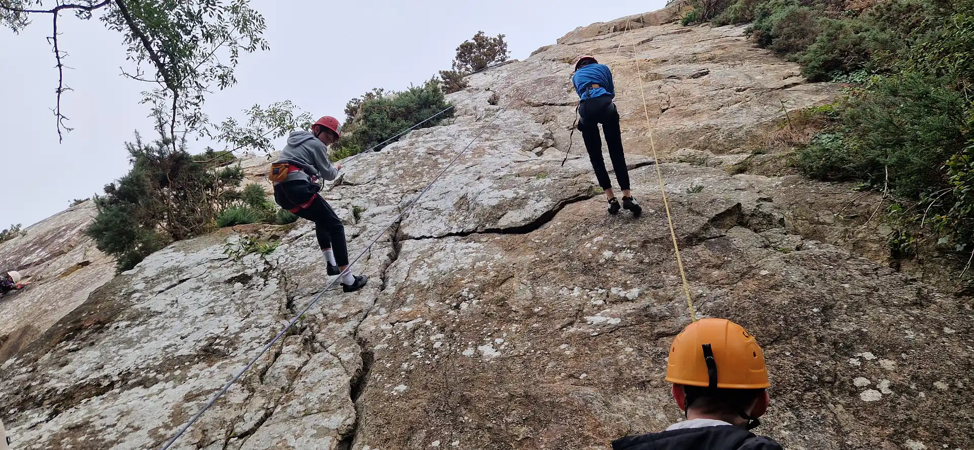 A view from the ground of two young climbers abseiling down real rock at Dalkey quarry in the Dublin Climbing Centre Outdoor Climbing Camp