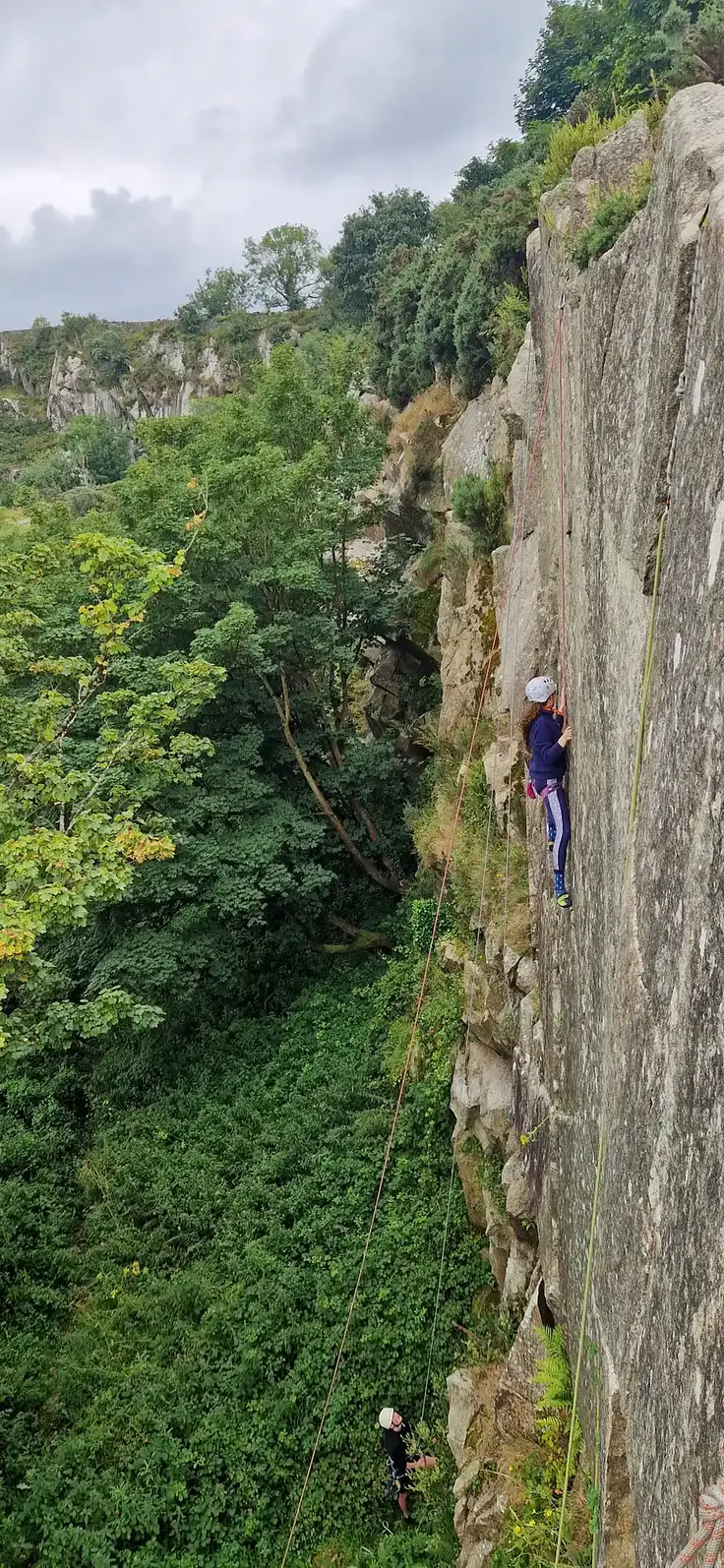 Instructor coaching a young climber on a vertical granite outdoor route at Dalkey quarry as part of Dublin Climbing Centre's outdoor climbing camp