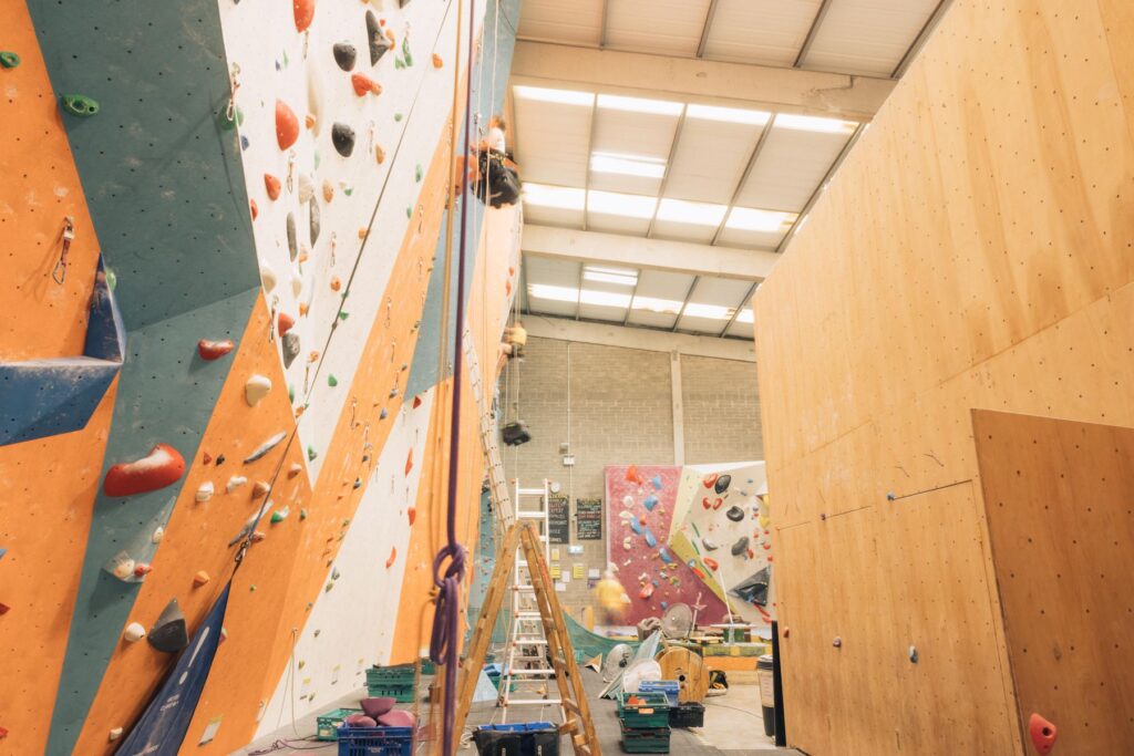 Route setter on a rope beside bouldering walls at Dublin Climbing Centre