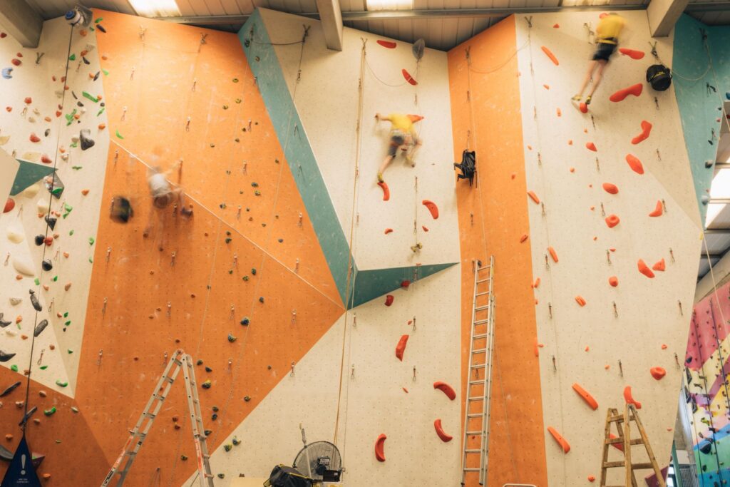Route setters working on an orange and teal lead climbing wall at Dublin Climbing Centre