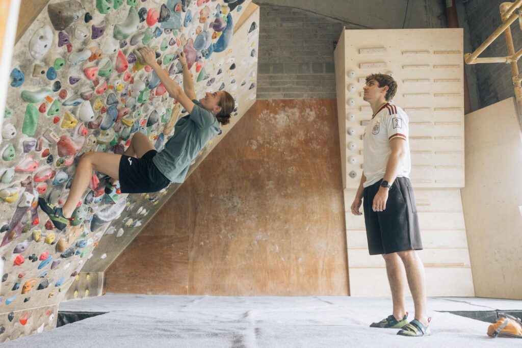 Climber bouldering on an overhang while a coach watches in the training room at Dublin Climbing Centre