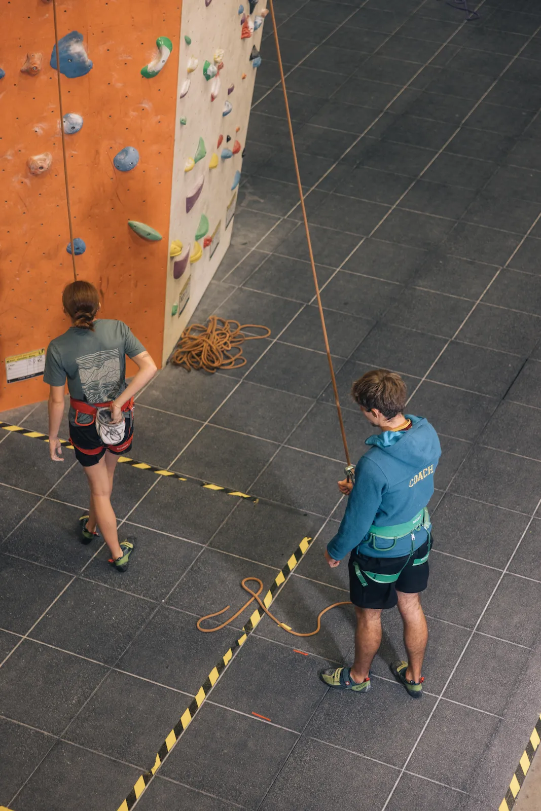 A Scout climber putting chalk on their hand and preparing to climb a route with their climbing instructor prepared to belay them at Dublin Climbing Centre